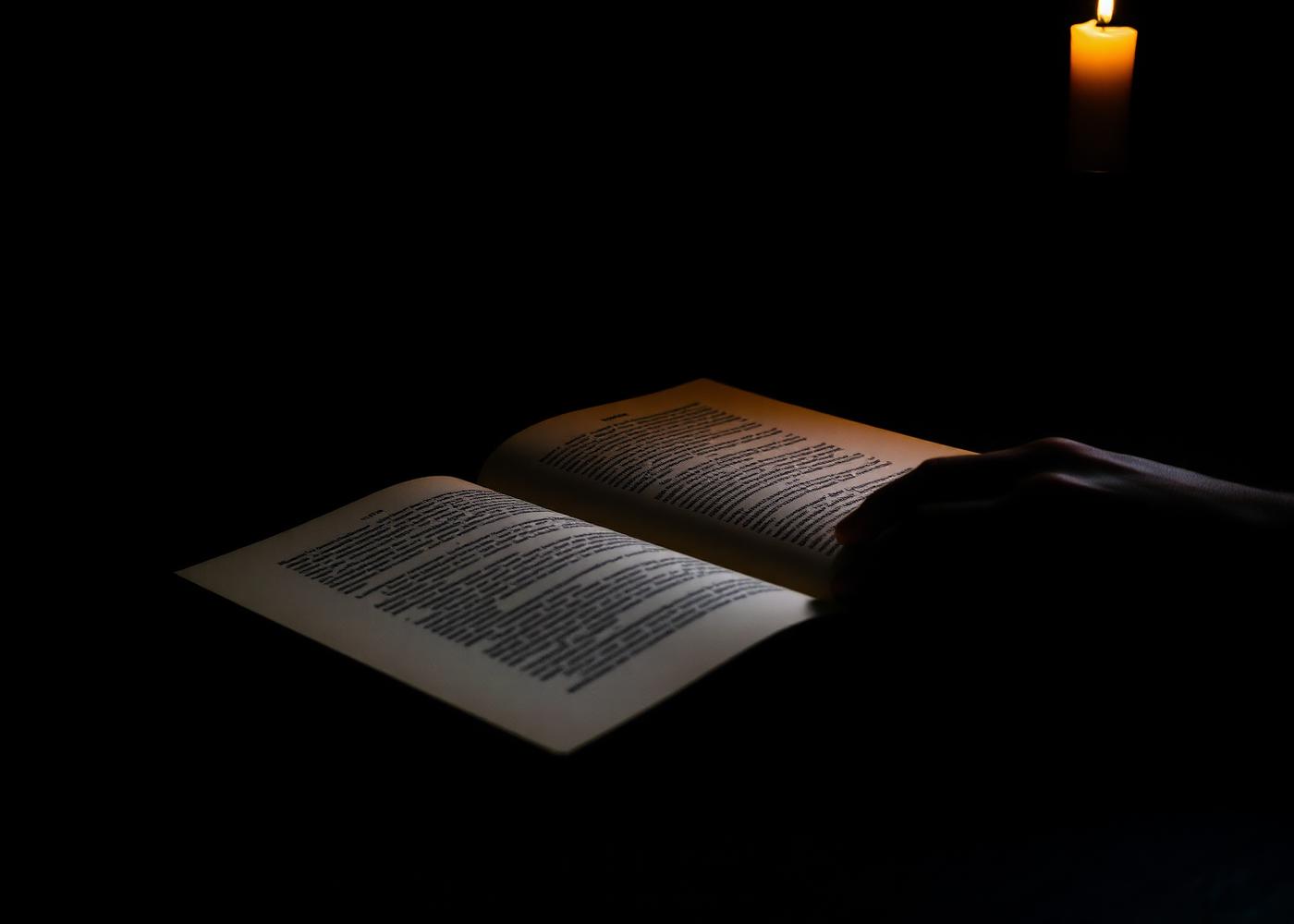 Main tournant les pages d'un livre d'art à la lueur d'une bougie